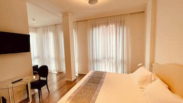 Una habitación de hotel con una cama grande, un escritorio con una silla y un televisor montado en la pared.