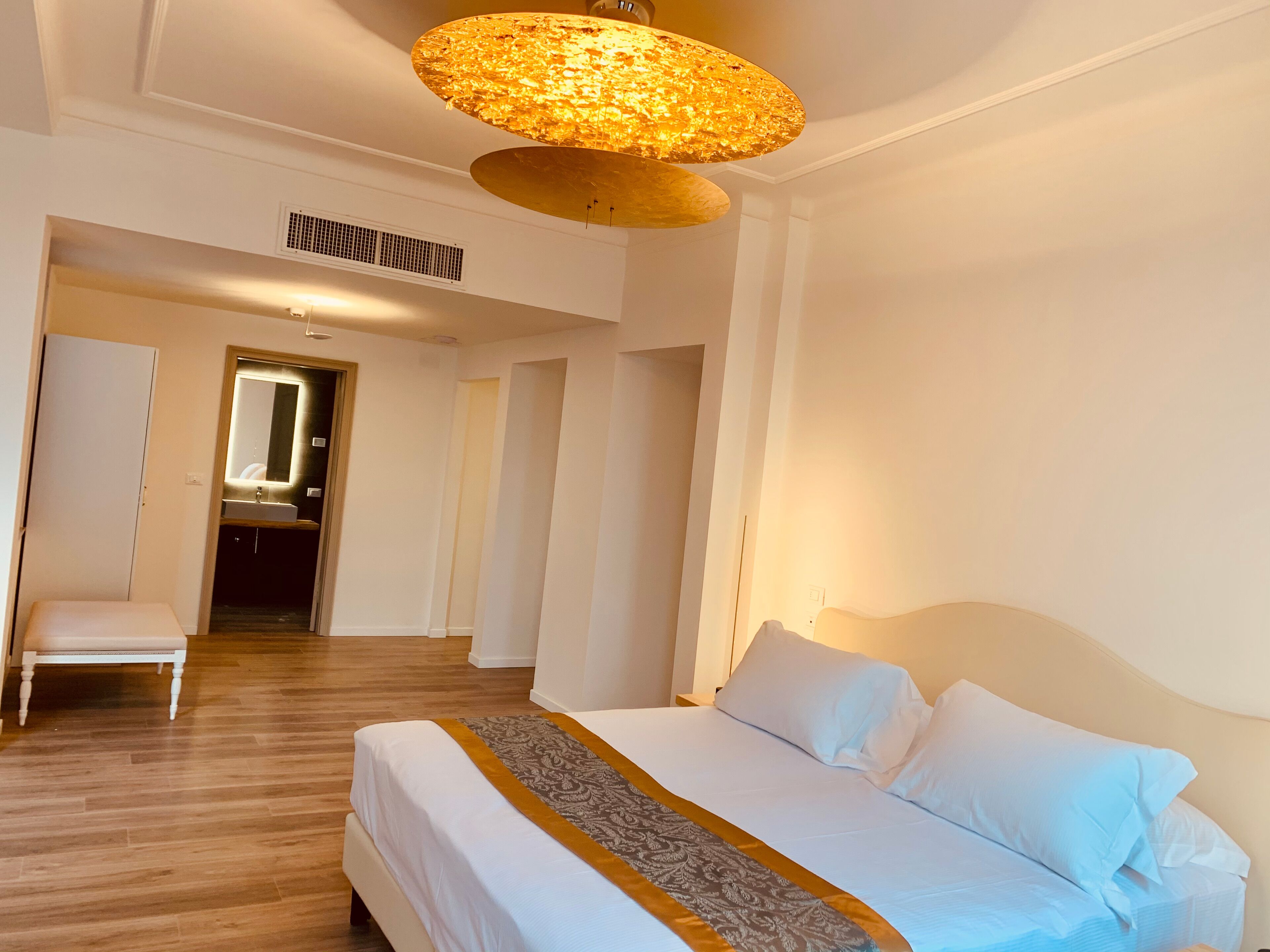 Una camera d'albergo con un letto grande, una zona salotto con una poltrona e un bagno visibile attraverso una porta aperta.