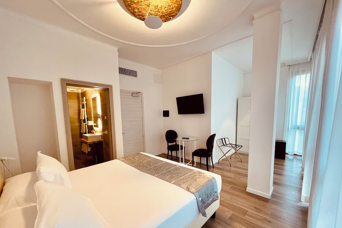 Ein Hotelzimmer mit Bett, Schreibtisch, Stuhl, Fernseher und einem sichtbaren Badezimmer durch eine offene Tür.
