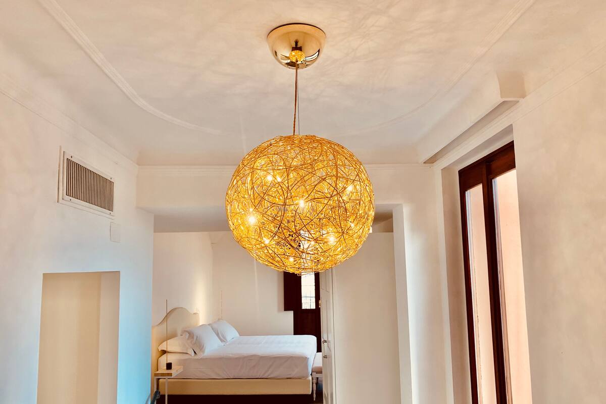 Ein Schlafzimmer mit einer großen, kugelförmigen, aufwendig gestalteten Pendelleuchte, einem Bett mit weißen Bettwäsche und einem Holzboden.