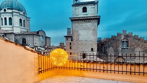 Una terrassa al terrat amb una decoració esfèrica de llum, una tanca metàl·lica i vistes a edificis històrics.