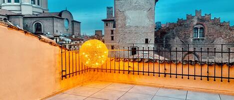 Una terraza en la azotea con una lámpara esférica decorativa, suelo de baldosas y vistas a edificios históricos, incluyendo una iglesia y una torre.