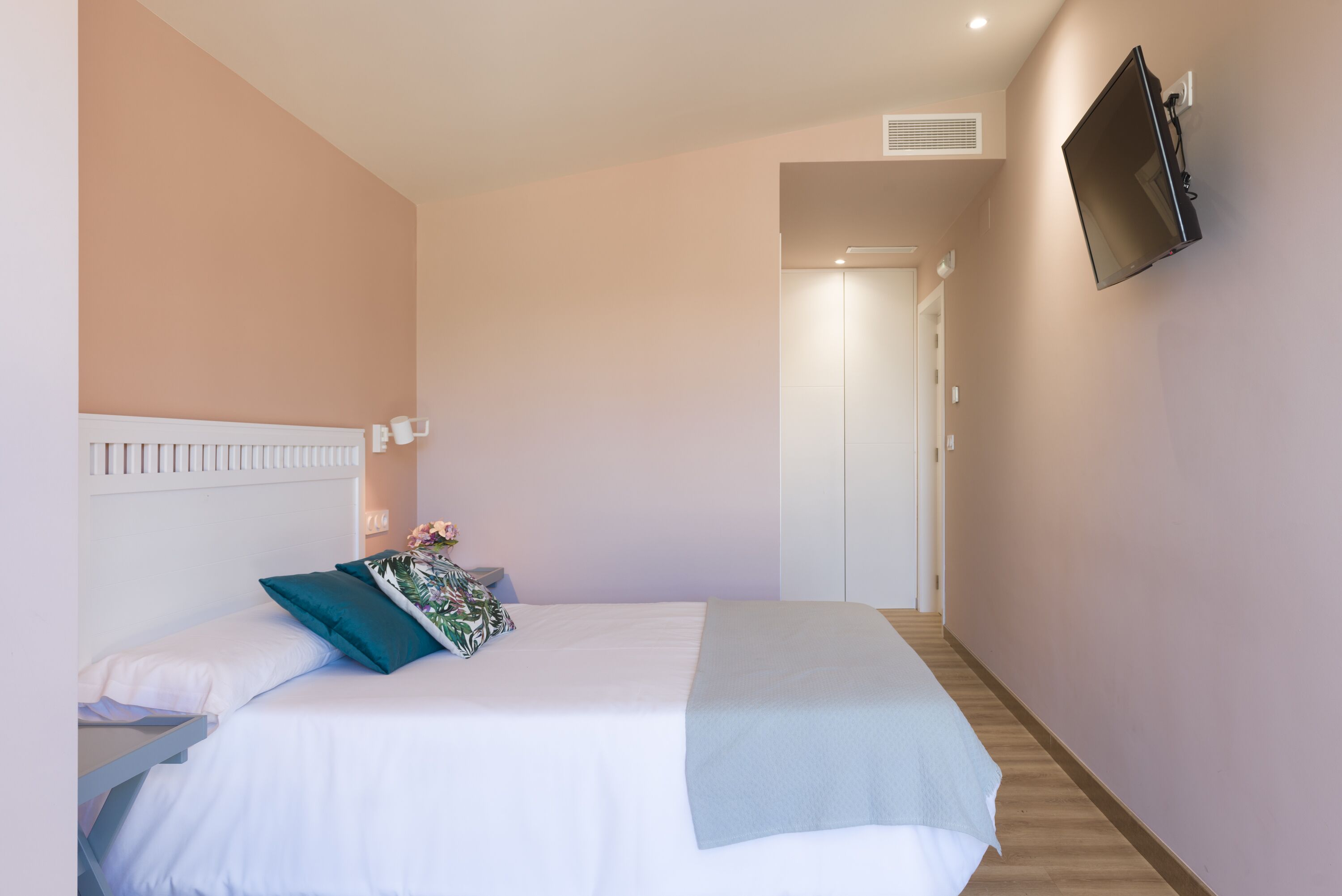 Ein Schlafzimmer mit einem Bett, einem an der Wand montierten Fernseher und einer Tür zu einem anderen Raum.