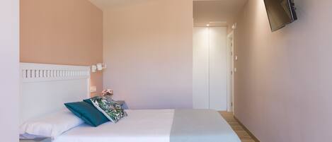 A bedroom with a bed, a TV mounted on the wall, and a door leading to another room.