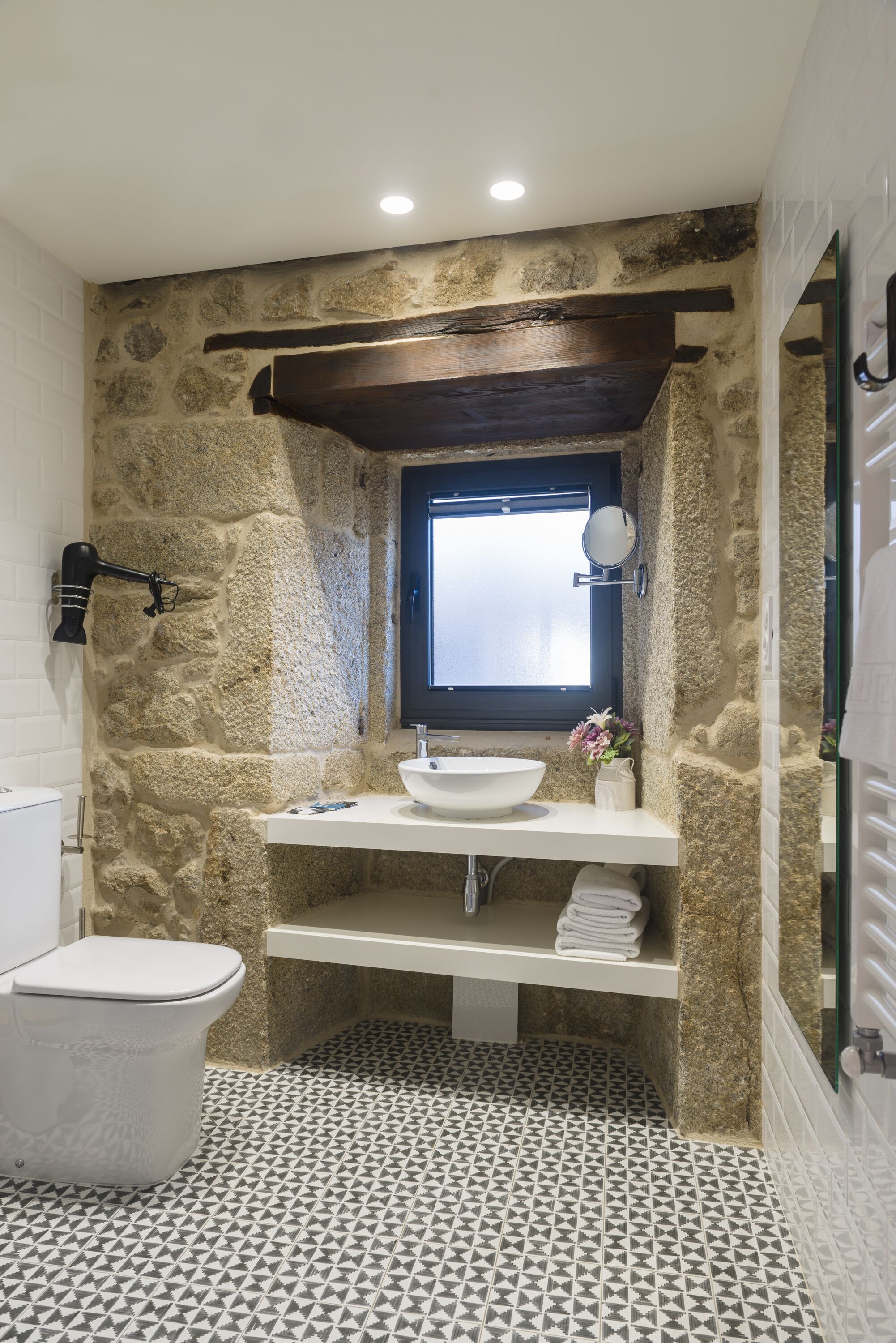 Un baño con pared de piedra, un lavabo blanco, un espejo y una ventana.