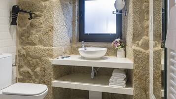 Un baño con pared de piedra, un lavabo blanco, un espejo y una ventana.