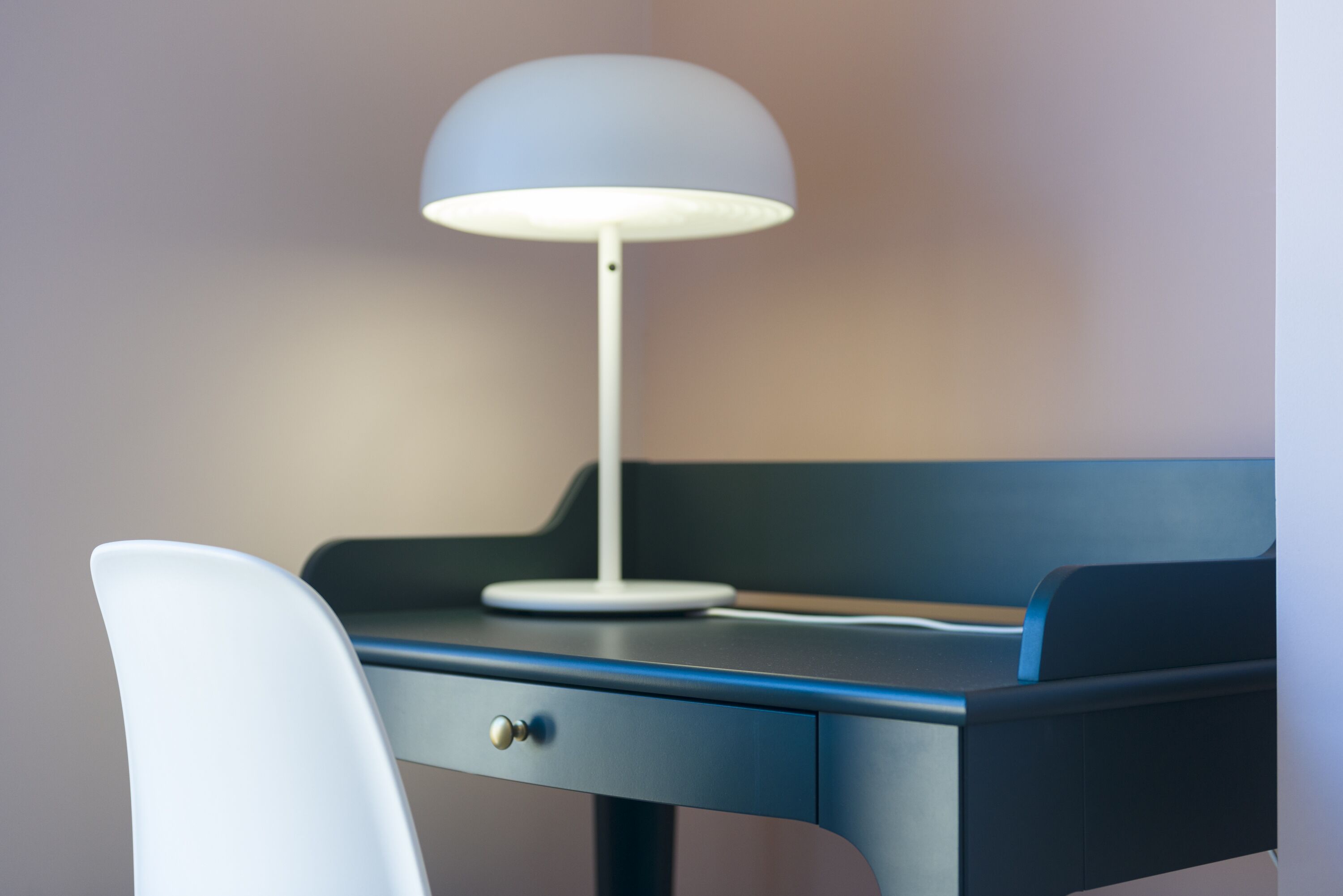 Een bureau met een lamp, een stoel en een lade.