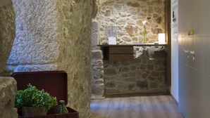 Un pasillo con paredes de piedra, un banco de madera y una pequeña mesa con una planta.