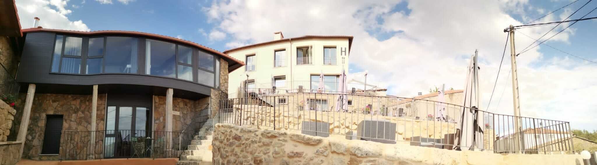 Un edificio de varios pisos con fachada de vidrio curvo, base de piedra y un balcón con barandillas.