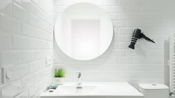 A bathroom with a white sink, a round mirror, a hairdryer mounted on the wall, and a potted plant on the counter.