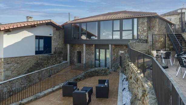 Un edificio de piedra de dos pisos con un patio amoblado y un muro de contención de piedra.