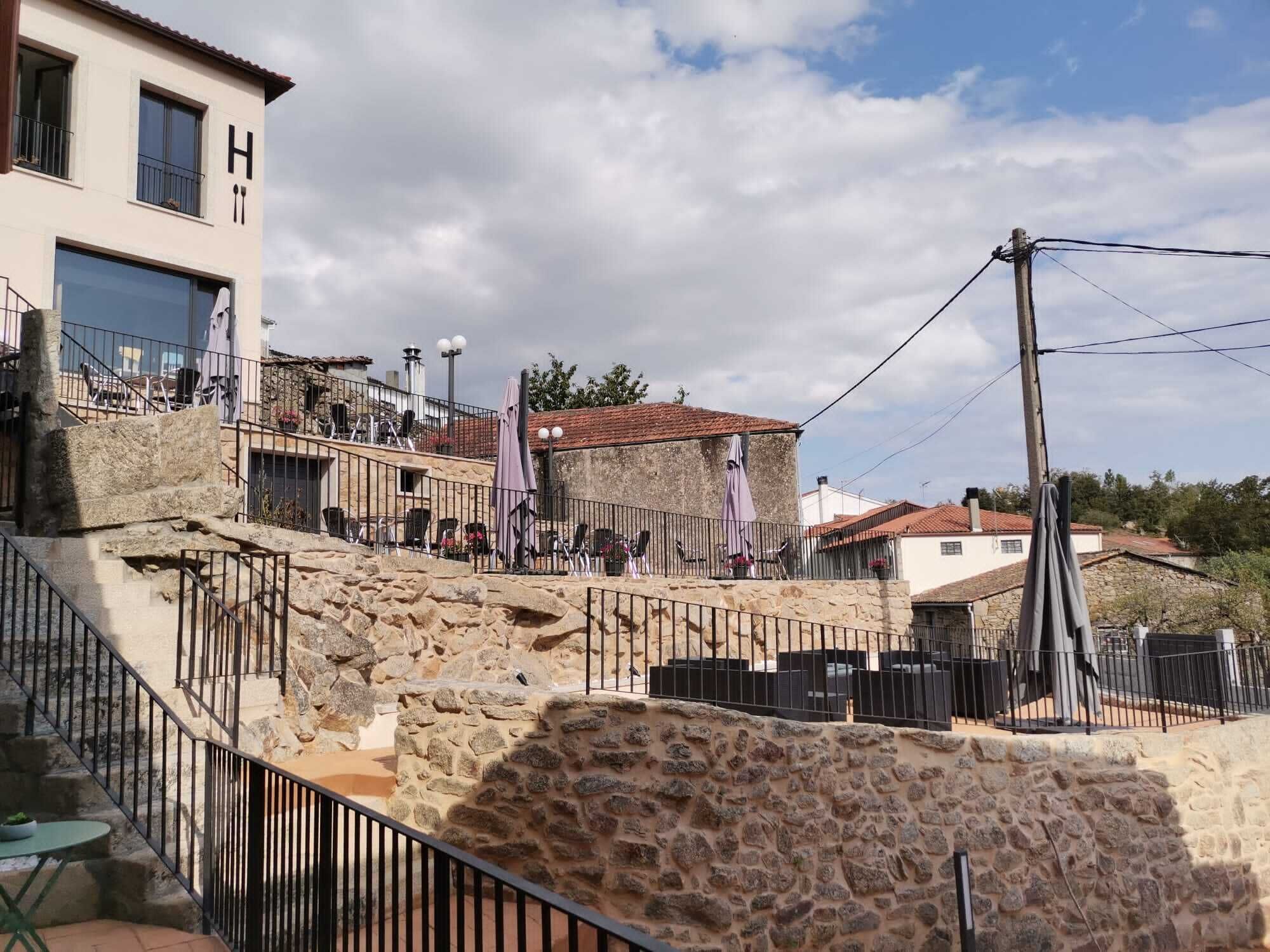 A stone staircase leading to a building with a 'H' sign, outdoor seating, and a stone wall.