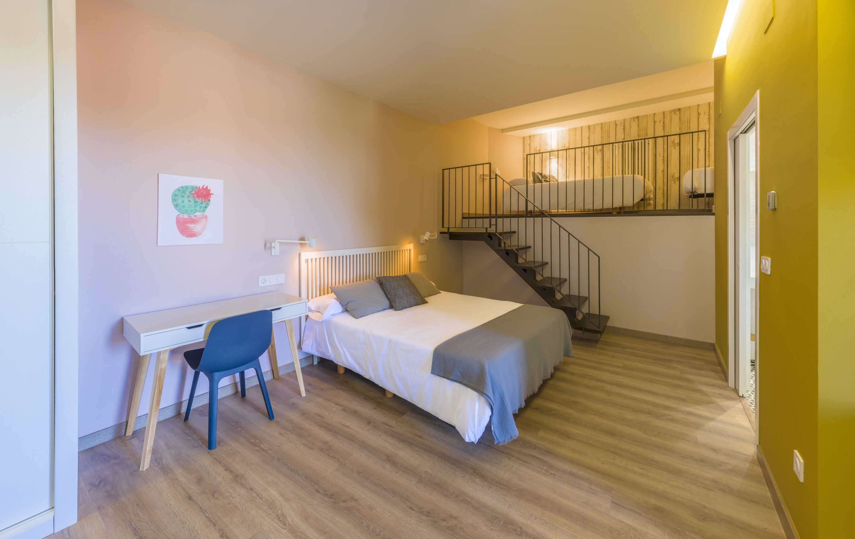 Un dormitorio con cama, escritorio, silla y una escalera que sube a un nivel superior.