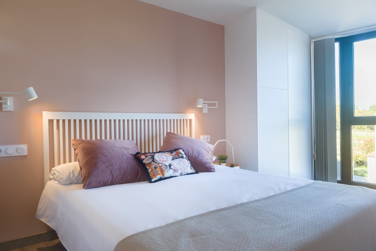 Une chambre à coucher avec un lit, deux oreillers, une table de chevet, une lampe et une fenêtre.