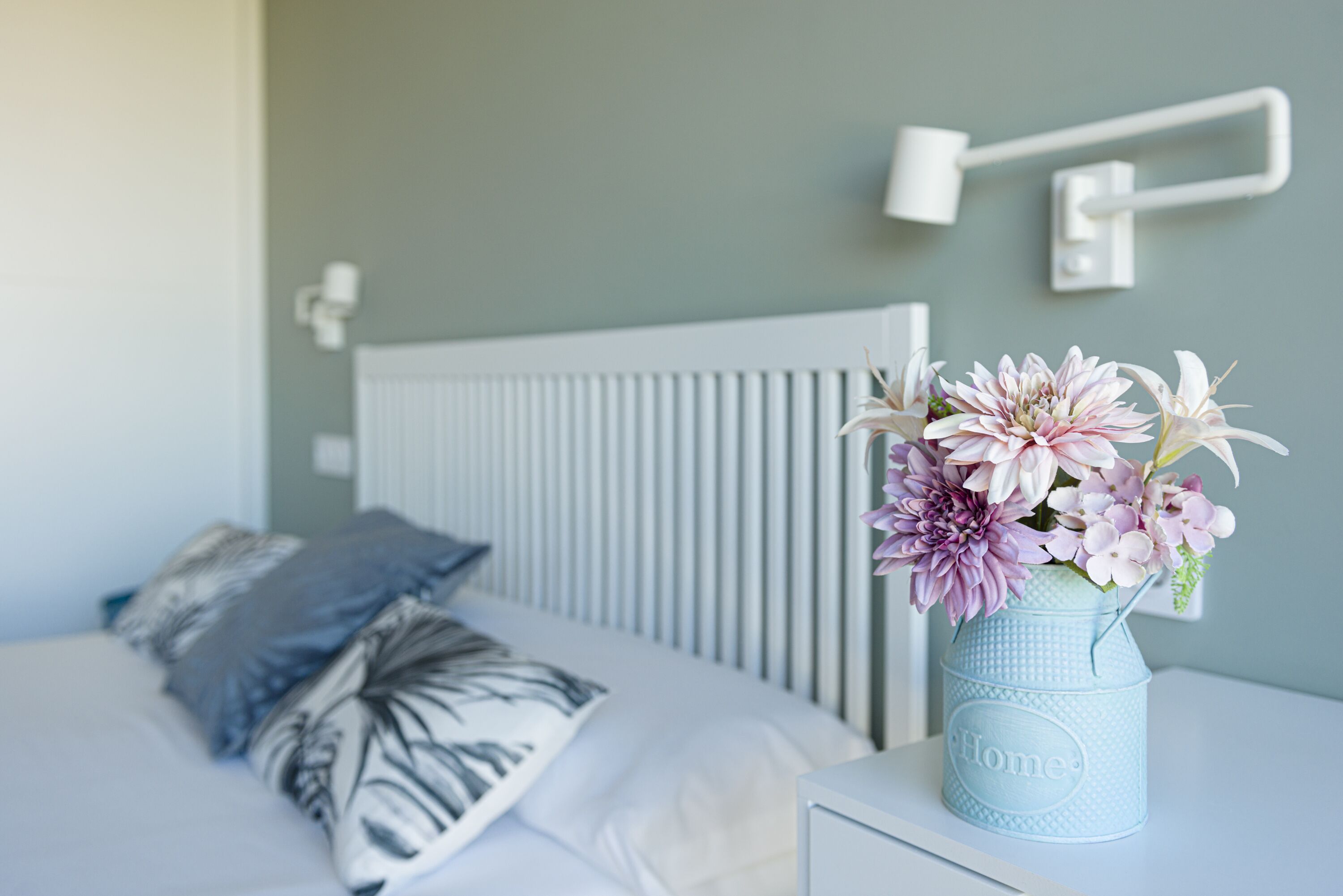 Un dormitorio con una cama, almohadas, una mesita de noche y un jarrón con flores.