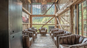 A rustic wooden interior with leather chairs arranged in rows, large windows, and a wooden ceiling structure.