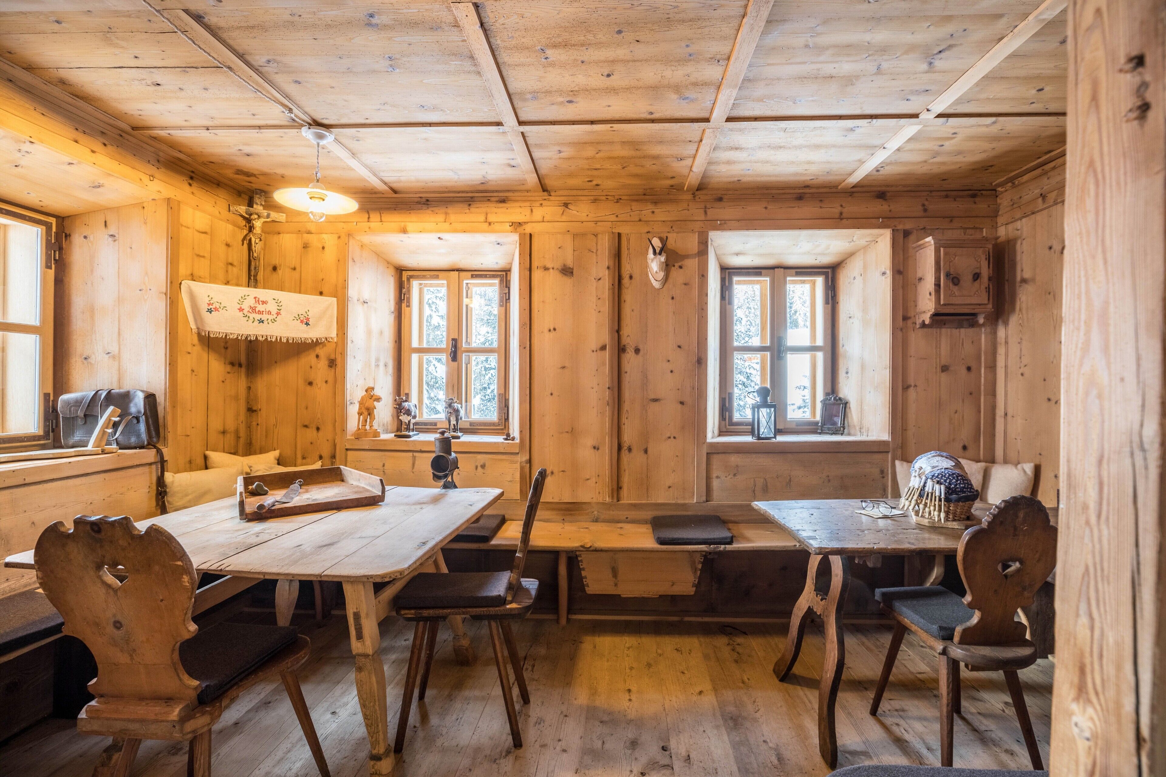 Interior de una cabaña de madera con una mesa de comedor, sillas, un banco y un estante en la pared.
