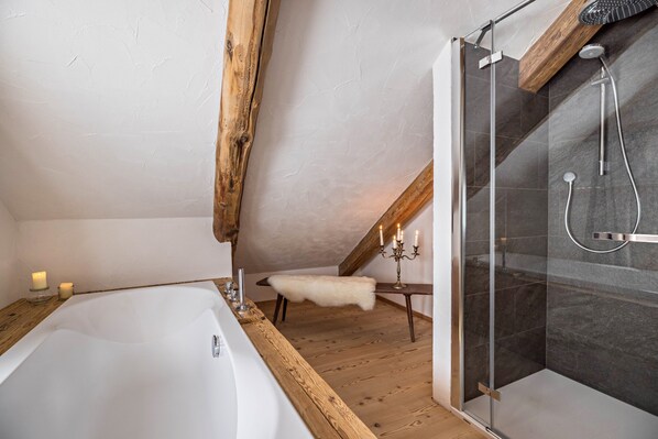 A modern bathroom with a bathtub, a glass-enclosed shower, wooden beams, and a small bench.