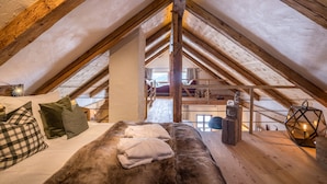 Ein Schlafzimmer im Dachgeschoss mit hohen Decken, Holzbalken, einem Bett mit Kissen, einem Fellteppich und einer Laterne.