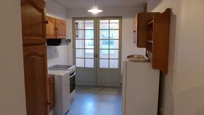 A narrow kitchen with wooden cabinets, a washing machine, a refrigerator, and a double door leading outside. - La Calypso the 2-person studio (+ 1 child under 3) ideal for fishing (Blangy-sur-Bresle)