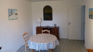 A dining area with a round table, chairs, a lamp, a painting, and a door. - La Calypso the 2-person studio (+ 1 child under 3) ideal for fishing (Blangy-sur-Bresle)