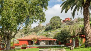 Un bâtiment à toit rouge doté d’une piscine, entouré d’une végétation luxuriante et de palmiers.