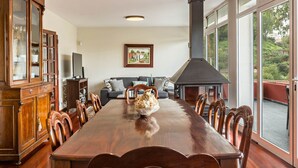 Une salle à manger avec une table en bois, des chaises, un buffet, une cheminée et un canapé avec des coussins.