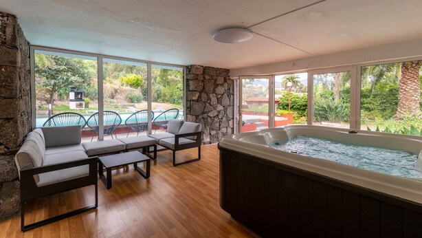 Une pièce avec un mur en pierre, un jacuzzi et une vue sur une piscine et un espace verdoyant.