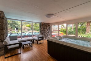 Una habitación con pared de piedra, un jacuzzi y vistas a una piscina y follaje.