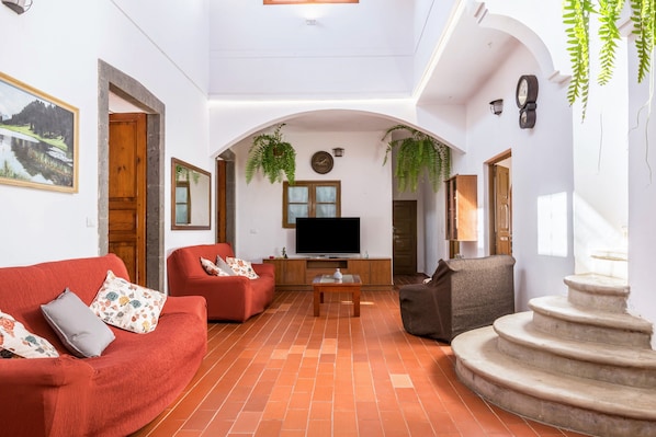 A spacious living area with a red sofa, a brown armchair, a television, and a stone staircase.