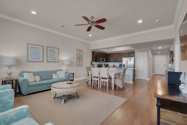 A spacious living area with a sofa, coffee table, and dining table. There is a kitchen in the background with cabinets and appliances.