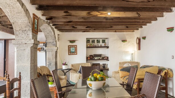 A dining area with a glass table, wicker chairs, a bowl of fruit, and a rustic stone archway. - Holiday Home "Casa Pollo Buen Lugar" with Rustic Charme & Terrace (Buenlugar)