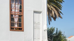 A white building with a window and door, a palm tree, and a clear blue sky. - Holiday Home "Casa Pollo Buen Lugar" with Rustic Charme & Terrace (Buenlugar)