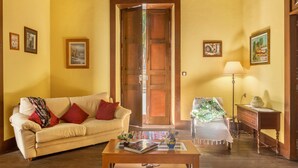 A room with a sofa, a coffee table with books, a lamp, and a bed with a green and white patterned bedspread. - Holiday Home "Casa Pollo Buen Lugar" with Rustic Charme & Terrace (Buenlugar)