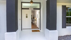 Een huisgevel met een witte deur, een klein voortuintje en een hangende lamp.