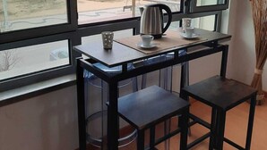 A room with a large window overlooking a beach and cliffs, a small table with a kettle, a cup, and a saucer, and a broom in a vase. - DUPLEX facing the sea, ideal for your family vacation (Nazaré)