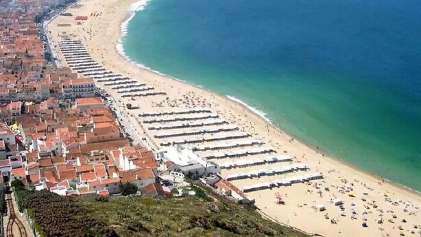 A coastal town with a long beach lined with rows of beach umbrellas and sun loungers. - DUPLEX facing the sea, ideal for your family vacation (Nazaré)