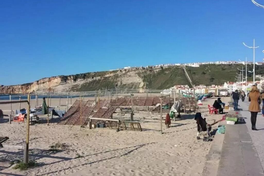 A beach with sun loungers, a few people, and a distant view of a town on a hill.