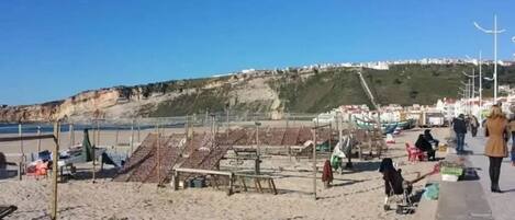 A beach with sun loungers, a few people, and a distant view of a town on a hill.