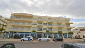 A multi-story hotel with a flat facade, several balconies, and a parking area with cars. - DUPLEX facing the sea, ideal for your family vacation (Nazaré)
