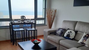 A modern living room with a sofa, a coffee table, and a dining area with chairs and a table. - DUPLEX facing the sea, ideal for your family vacation (Nazaré)