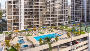 A multi-story hotel with a rooftop pool area, lounge chairs, and a parking garage. - Deluxe Condo with Recreation Deck View, Free parking & WiFi (Honolulu)