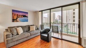 A living room with a grey sofa, a black chair, and a painting of a cityscape. - Deluxe Condo with Recreation Deck View, Free parking & WiFi (Honolulu)