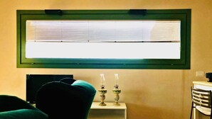 A room with a large window, a white side table with decorative items, and a chair.