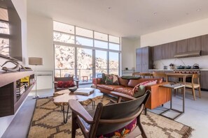 A spacious living area with a large window, a sofa, a coffee table, and a kitchen area with cabinets and a stove.