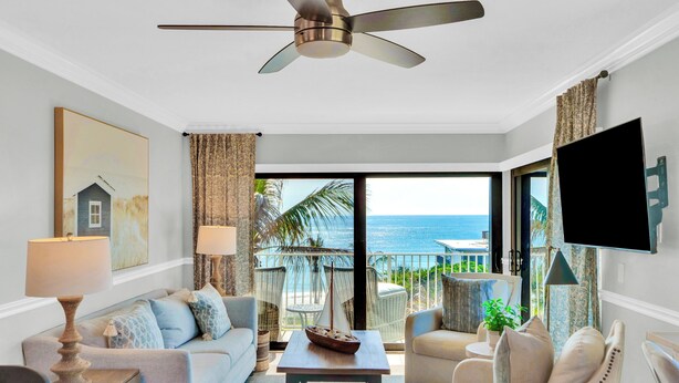 Un salon avec un ventilateur de plafond, un canapé, une table basse et un téléviseur fixé au mur.