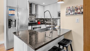 A modern kitchen with a stainless steel refrigerator, a built-in coffee maker, a large island with a sink, and a wine rack on the wall. - Seascape Amenities☀️Pools~Coastal Cottage⛱️ (Miramar Beach)
