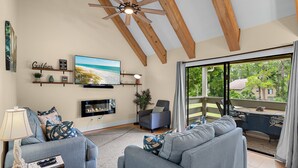 A living room with a sofa, a TV, a ceiling fan, and a balcony with a table and chairs. - Seascape Amenities☀️Pools~Coastal Cottage⛱️ (Miramar Beach)