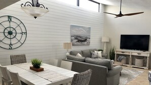 En moderne stue med spiseplads, en grå sofa, et fjernsyn og et vægur.