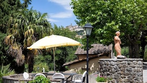 Ein Terrassenbereich mit Sitzgelegenheiten im Freien, einer Statue und einem gelben Sonnenschirm.